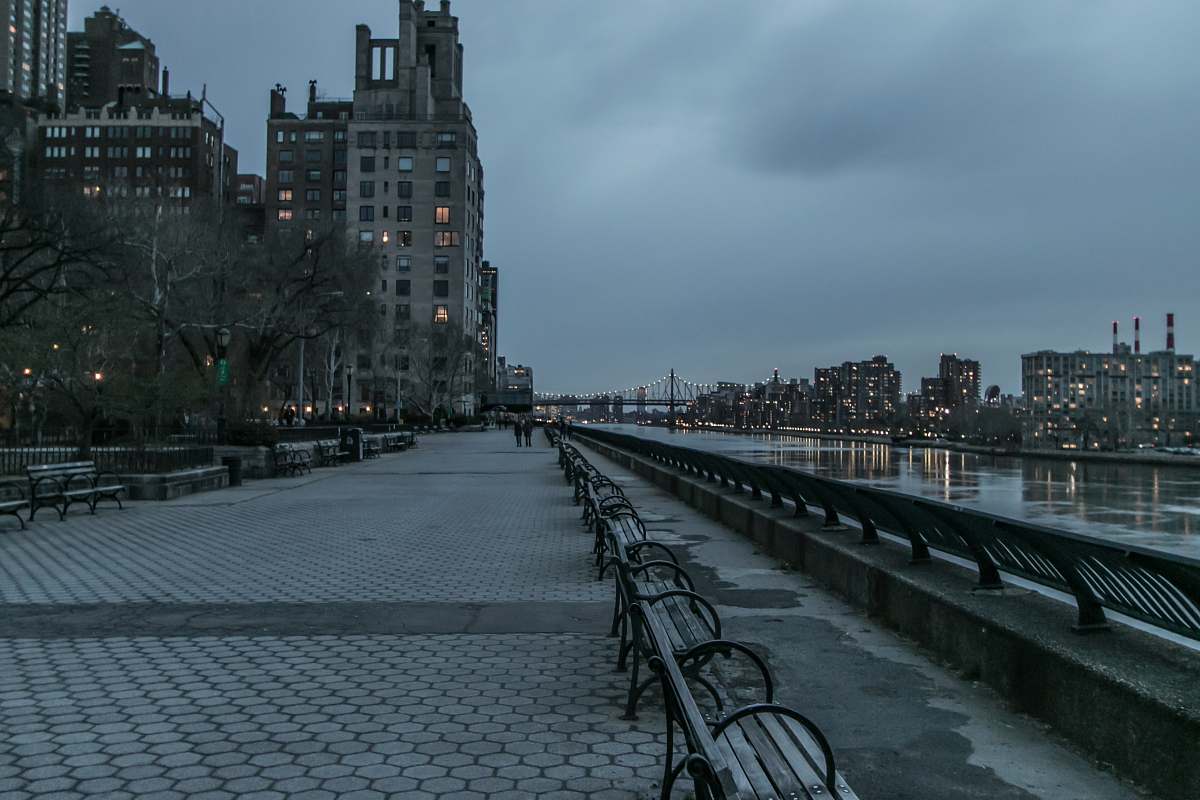 Discover the tranquility of Carl Schurz Park, a peaceful escape nestled in the heart of the city. This picturesque scene features an empty park set against a shimmering body of water, framed by stunning urban architecture. A row of inviting benches offers the perfect spot for contemplation or relaxation, making it an ideal backdrop for lifestyle photography, urban exploration themes, and serene nature imagery. Embrace the charm of city parks where nature meets architecture.